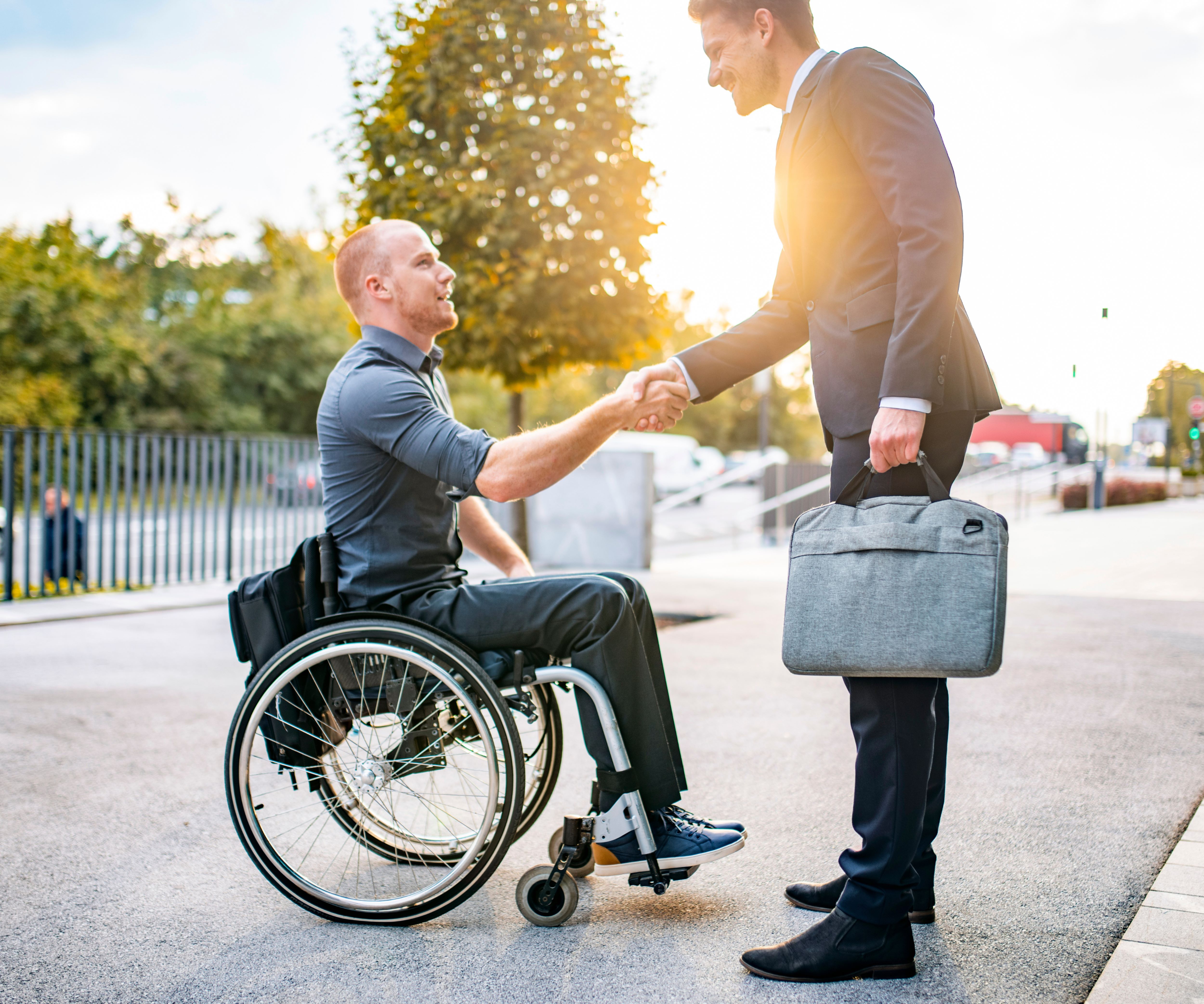 A student in a wheelchair shakes the hand of a standing man in a suit holding a briefcase