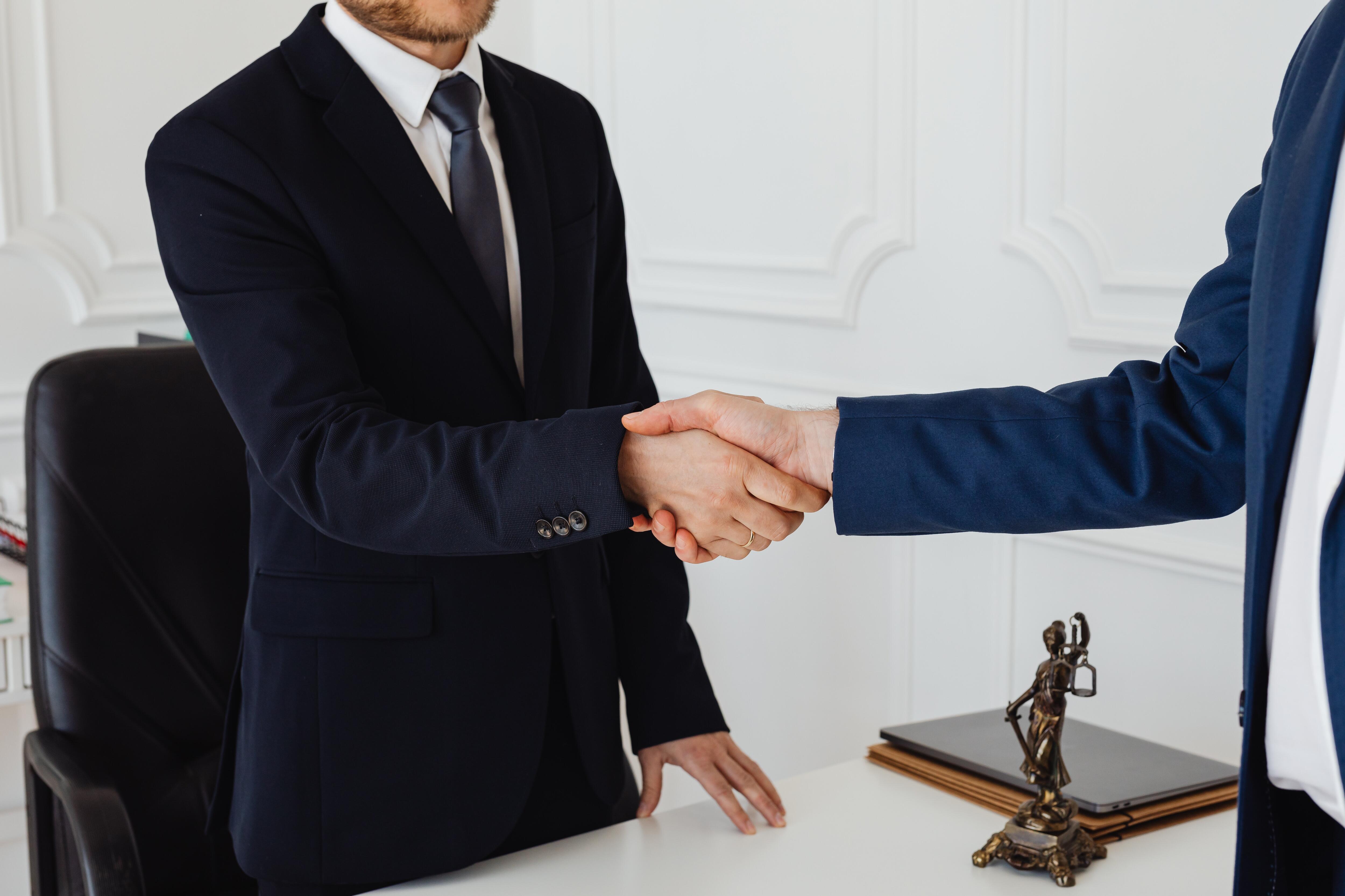 someone in a dark suit and tie shaking hands with someone else in a suit